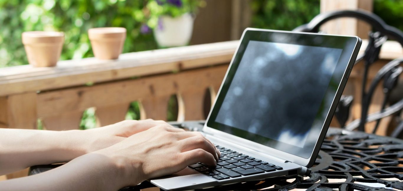 Eine Person tippt auf einem Laptop, während sie auf einer Terrasse sitzt.