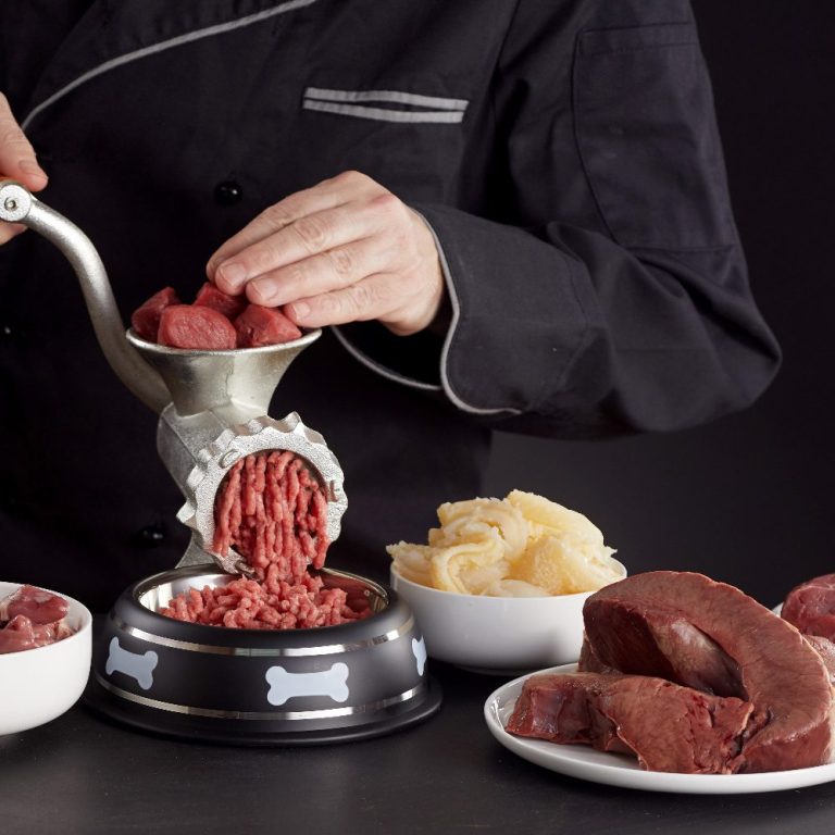 Ein Koch benutzt einen Fleischwolf, um frisches Fleisch zu mahlen, umgeben von rohem Fleisch.